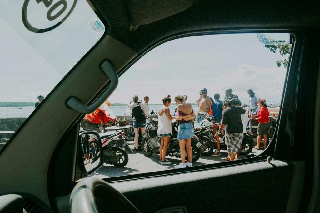 A group of friends socialize by the sea in Bali, Indonesia, near several motor scooters.